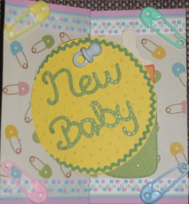 Baby card front
I used the Circle Flip It die to create a New Baby card. I used baby pin paper, then used the die to cut out a yellow for the circle.  The circle was trimmed with little green rickrack. I trimmed the top and bottom of the card with ribbon and added a plastic diaper pin in each corner. The New Baby words is from a Sizzix Slizzlit - Phrase, new Baby w/Onesie. I added a plastic baby pacifier above the words. The green sticking out on the bottom right corner is the inside bottle.
Keywords: Circle Flip It die sizzlit newBaby w/Onesie